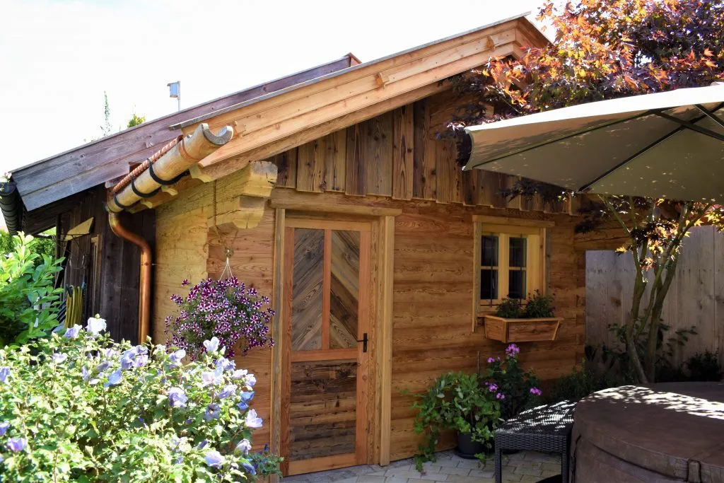 Frontansicht eines Gartenhauses aus Holz, Garten mit Bepflanzung im Vordergrund