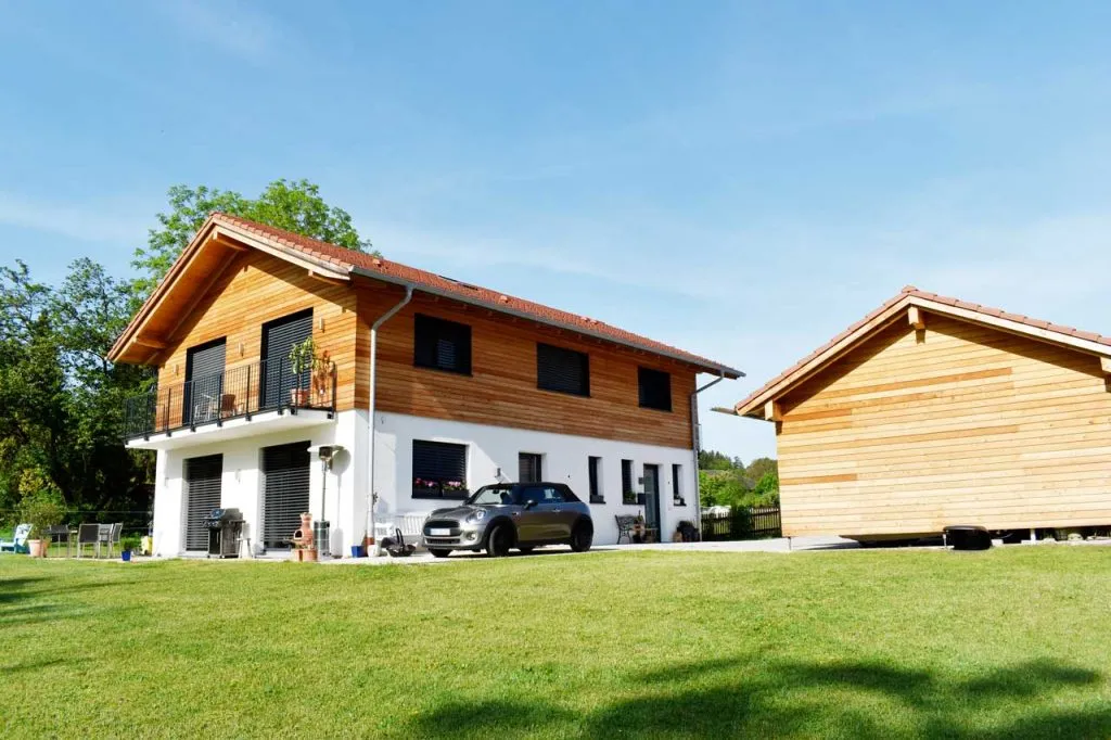 Modernes Haus mit Holzfassade und Balkon, Carport und Grünfläche bei sonnigem Wetter